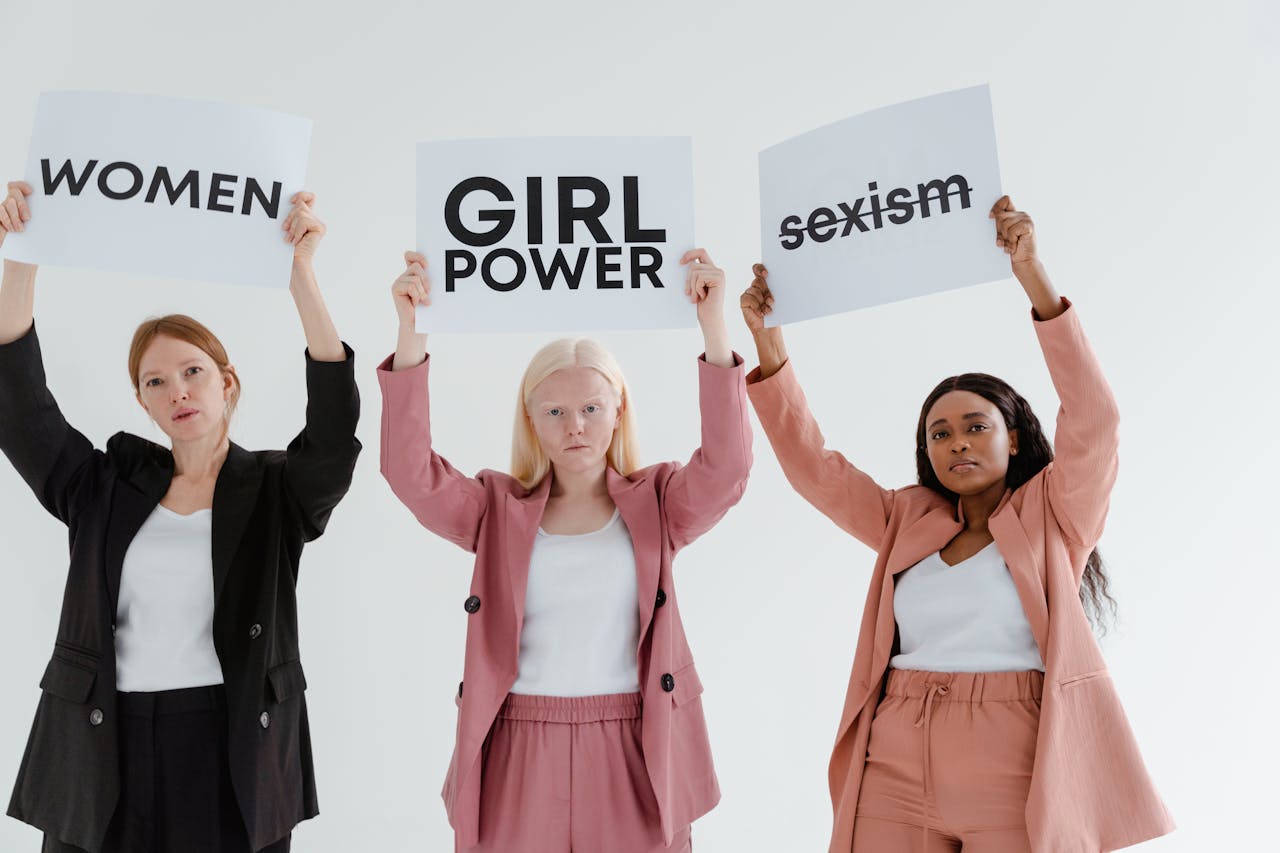 Three women holding empowering signs promoting feminism and tackling sexism.